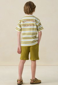 T-shirt rayé blanc, jaune et vert avec le texte "PROFITEZ DU SOLEIL", associé à un short vert texturé et des sandales marron clair.
