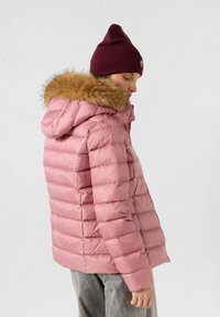 Giacca a vento rosa con motivo a righe orizzontali, cappuccio foderato in pelliccia e zip frontale. Abbinata a un berretto color bordeaux.