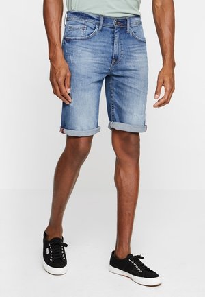 Pantaloni corti in denim blu da uomo con una finitura sbiadita. Presentano risvolti, cinque tasche e una chiusura con cerniera. Indossati con sneakers nere.