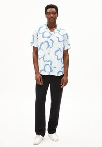 Korte mouwen shirt met een lichtblauw en wit abstract patroon, voorzien van een zak en een losse pasvorm, gecombineerd met zwarte broek en witte sneakers.