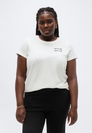 Kobieta z warkoczem, ubrana w biały t-shirt z napisem "OUT OF OFFICE" oraz czarne spodnie, stoi na tle jasnej, jednolitej ściany.