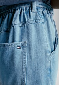 Pantaloni di denim azzurro chiaro con vita elastica, tasche laterali e una piccola toppa ricamata con logo in rosso, bianco e blu.