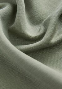 Grüner Stoff mit einer weichen Textur, der ein feines Strickmuster zeigt. Das Material fällt glatt und präsentiert sanfte Farbvariationen.