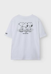 Camiseta blanca de manga corta que presenta tres ilustraciones de Snoopy en la parte de atrás, con el texto "SOLO BUENAS VIBRACIONES" abajo.