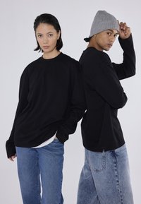 Cămășile negre cu mânecă lungă au un croi lejer, cu manșete striate și fante laterale, fiind asortate cu blugi din denim de culoare albastru deschis. Unul dintre modele poartă o căciulă gri.