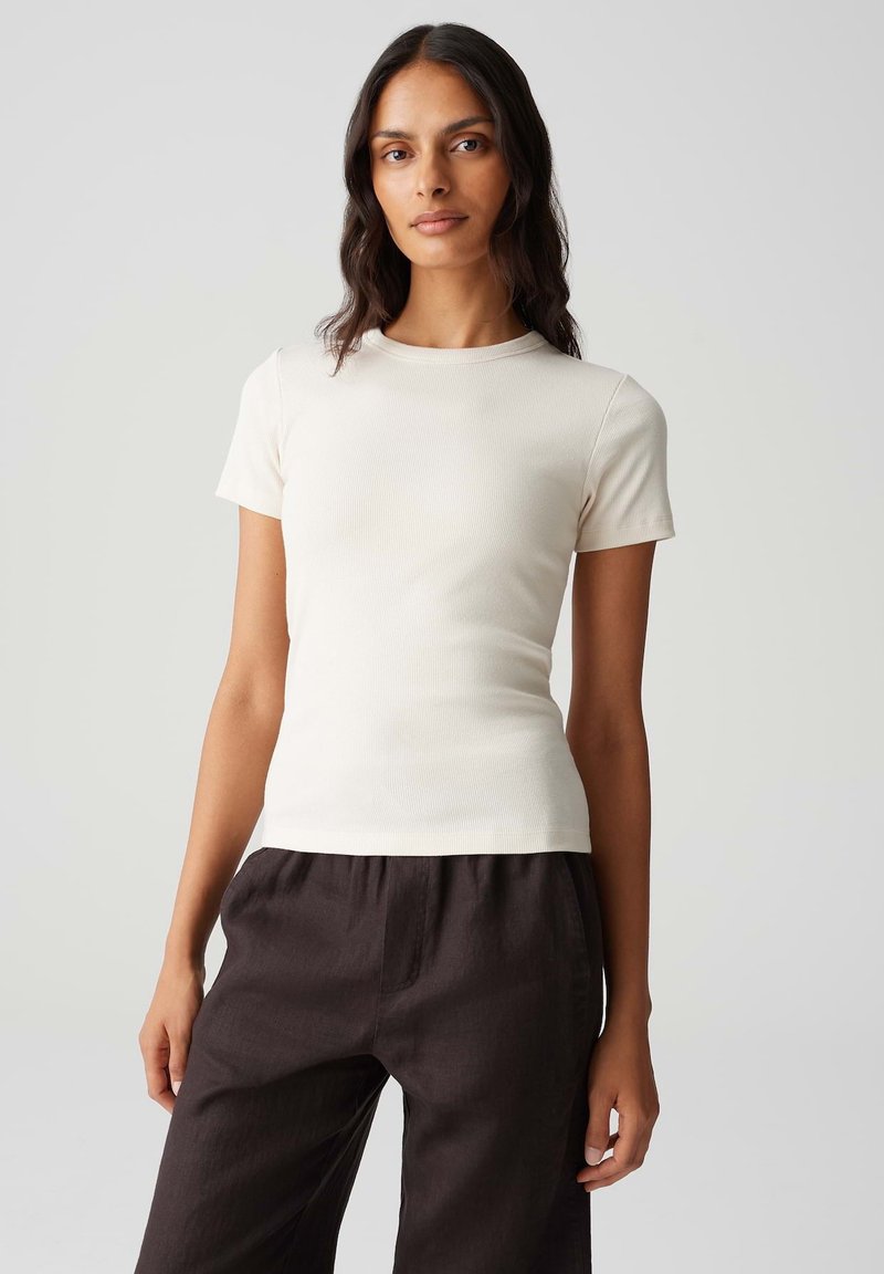 T-shirt fitted color crema con maniche corte, texture a coste e scollo rotondo, abbinata a pantaloni scuri e larghi.