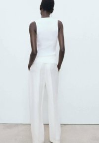Top bianco senza maniche e pantaloni bianchi a vita alta. Tessuto a maglia liscia, vestibilità sartoriale e leggero pieghettato sulla schiena.