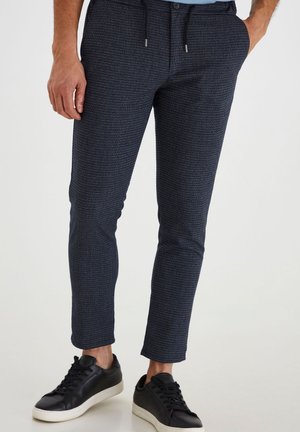 Navy patterned trousers with a textured fabric, featuring an elastic waistband with drawstrings. Paired with black sneakers.
