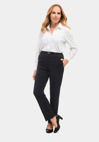 Witte lange mouwen shirt, donkere marineblauwe broek met elastische tailleband en zwarte hoge hakken. Glad materiaal met een getailleerde pasvorm.