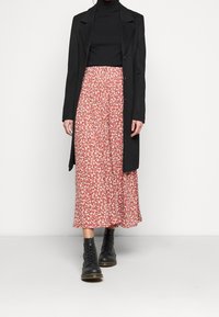 Black long coat over a black turtleneck, paired with a red floral midi skirt featuring a button front, and black lace-up combat boots.