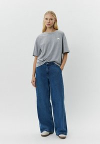 Camiseta gris de manga corta con un pequeño parche de logo, combinada con jeans de mezclilla azul de pierna ancha, diseño minimalista y un estilo casual y limpio.