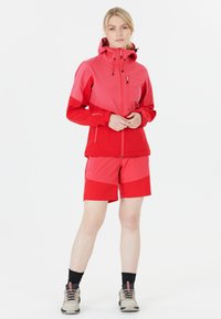 Röd och rosa jacka med huva, texturerat tyg och blixtlås. Matching röda shorts. Grå vandringsskor med svarta detaljer.