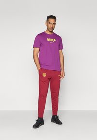 Violeta T-kreklu ar dzelteno "BARÇA" tekstu un Nike logo, apvienojot ar sarkanām biksēm, kurām ir dzeltenais kluba logo un Nike emblēma, valkātās ar melniem apaviem.