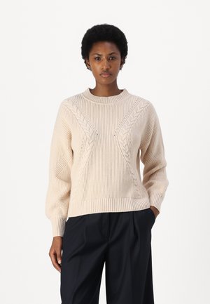 Pull en tricot couleur crème avec une texture côtelée, présentant un motif en torsades sur le devant et un col rond.