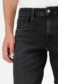 Jeans in denim nero con una vestibilità slim, dotati di tasca anteriore e chiusura con bottone. Il tessuto presenta una leggera trama sbiadita.