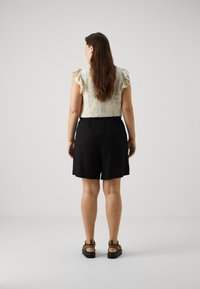 Blouse florale pour femmes avec des manches volantes, associée à des shorts avec ceinture élastique noirs. Portée avec des sandales à brides marron.