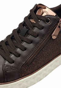 Sneaker marrone con tessuto testurizzato e parte superiore in pelle, con lacci marroni scuri, una cerniera laterale e una suola bianca a motivo diamante.