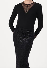 Haut noir à manches longues avec encolure en dentelle, associé à une jupe noire présentant un motif floral en velours et une texture lisse.