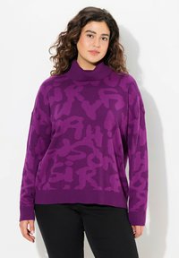 Pull en tricot violet avec un col montant et un motif abstrait en violet plus foncé, présentant des épaules tombantes ainsi que des poignets et un ourlet côtelés.