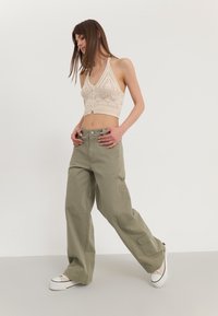 Haut halter beige en tricot avec des motifs en losange, associé à un pantalon cargo vert olive à coupe décontractée. Le mannequin porte des baskets à plateforme blanches.