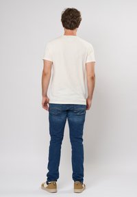 Kremfarget t-skjorte med kort erm, bakfra, kombinert med blå jeans. Mykt stoff, standard passform, enkelt design, ingen synlige logoer eller mønstre.