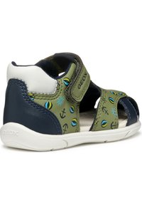 Sandały chłopięce z górną częścią z zielonej skóry, z wzorami kotwic i słońc, granatowymi akcentami, otwartą budową palców i białą gumową podeszwą. Zapięcie na rzep.