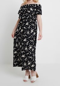 Czarna maxi sukienka bez ramiączek z białym kwiatowym wzorem, falbaniastego dekoltu oraz elastyczną talią, w zestawie z białymi sandałkami na obcasie.
