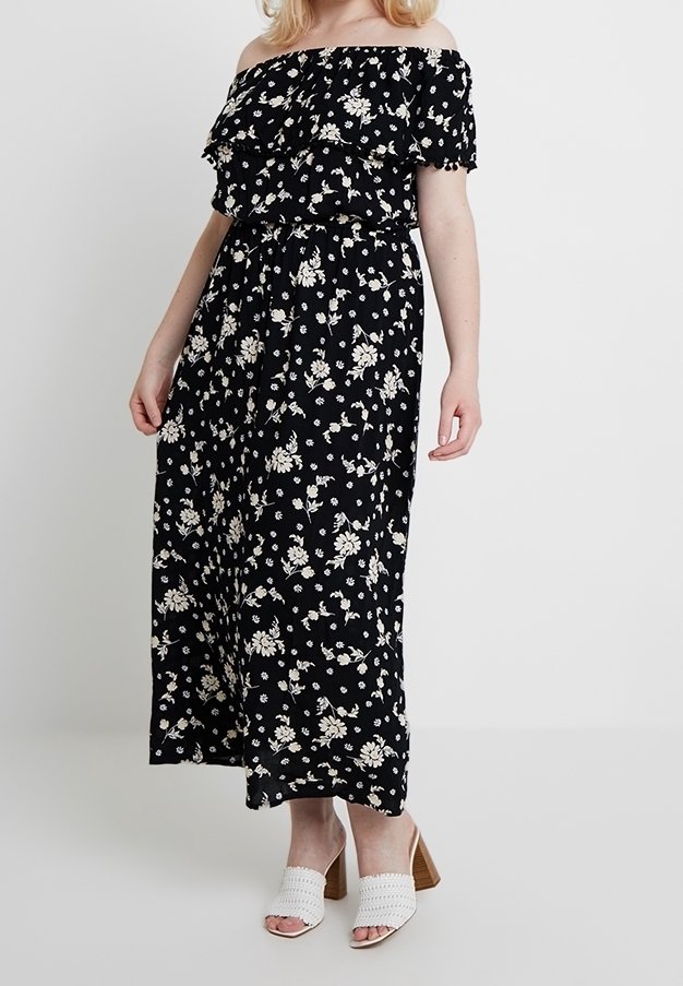 Czarna maxi sukienka bez ramiączek z białym kwiatowym wzorem, falbaniastego dekoltu oraz elastyczną talią, w zestawie z białymi sandałkami na obcasie.