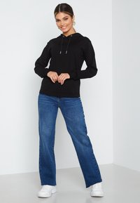 Felpa nera con cappuccio e cordini, abbinata a jeans svasati azzurri chiari e sneakers bianche. Tessuto morbido, design casual.