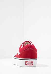 Czerwone zamszowe sneakersy z białym paskiem, czarną podeszwą i logo Vans na pięcie. Posiadają zaokrąglony czubek i wyściełany kołnierz.