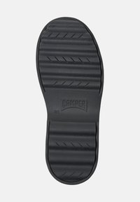 Suola di scarpa in gomma nera con scanalature orizzontali e un logo. Presenta una superficie liscia e bordi arrotondati, progettata per offrire aderenza e durabilità.