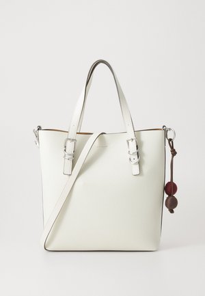 Sac à main en cuir blanc avec double poignées, bandoulière ajustable et amovible, et deux boules décoratives en laine marron et rouge sur l'anneau latéral.