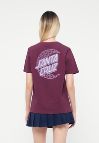Bordeaux bomull T-skjorte med et sirkulært grafisk motiv som har "Santa Cruz" i lys lilla og et geometrisk mønster. Korte ermer, rund hals.