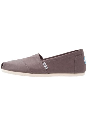 Scarpa slip-on in tela grigia con punta affusolata, caratterizzata da dettagli di cuciture diagonali e una suola in gomma bianca. Etichetta con logo sul lato.