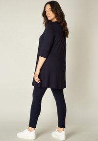 Marine tuniek met 3/4 mouwen, vloeiende ontwerp. Gecombineerd met slim-fit marine leggings en witte sneakers. Gladde textuur, eenvoudig, minimale details.