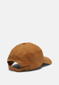 Brun bomulds-baseballcap med en buet skygge, justerbar strop bagpå og syningsdetaljer. Har et mærket metalaccent.