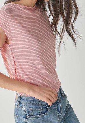 Frau trägt ein rosa-weiß gestreiftes ärmelloses Top und blaue Jeans, mit langen braunen Haaren, teilweise sichtbar.