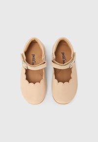 Ζευγάρι μπεζ παιδικά παπούτσια Mary Jane με κυματιστά άκρα και ασημένιες αγκράφες σε λευκό φόντο.