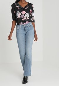 Blouse noire à motifs floraux rose et blanc ; se caractérise par un décolleté en V et une finition en dentelle. Assortie à un jean droit bleu clair et des bottes noires.