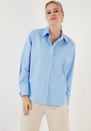 Light blue button-up shirt in cotton fabric, featuring a classic collar, long sleeves, and a relaxed fit with a curved hemline.