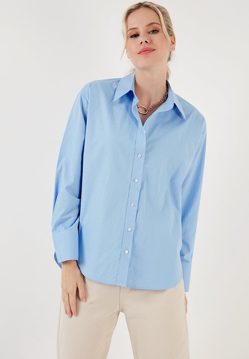 Light blue button-up shirt in cotton fabric, featuring a classic collar, long sleeves, and a relaxed fit with a curved hemline.