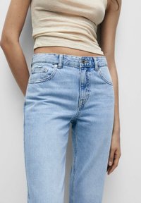 Jeans in denim blu chiaro con vita alta, design a cinque tasche e una texture leggermente sbiadita. Presentano una chiusura a bottoni metallici e zip.