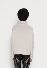 Ljusbeige polotröja med ribbstickade muddar och fåll. Mjuk textur, avslappnad passform och minimalistisk design. Matchas med svarta byxor i konstläder.