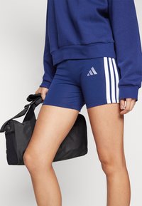 Shorts sportivi blu navy con strisce bianche, dotati di logo Adidas. Il materiale è elastico e aderente, con una consistenza liscia.