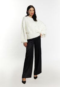 Pulover alb supradimensionat cu fir texturat si embellishments cu perle, asortat cu pantaloni largi din satin negri si pantofi cu toc ascuțit negri.