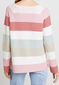 Persona che indossa un maglione a maniche lunghe in maglia con righe orizzontali nei colori rosa, rosso, bianco, azzurro e beige, abbinato a jeans azzurri.