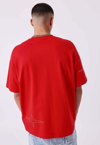 Rode T-shirt met korte mouwen en een losse pasvorm, voorzien van een stervormige stikseldetail nabij de zoom. Gemaakt van gladde stof met een eenvoudige ontwerp.