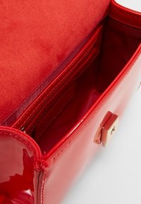 Borsa a mano in vernice rossa con texture liscia, chiusura in metallo dorato e un ampio interno foderato in tessuto con scomparti per carte.