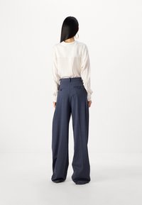 Cremefarbige Bluse mit einem Rückennahtdetail, kombiniert mit weiten, marineblauen Hosen mit Gesäßtaschen und taillierter Passform.