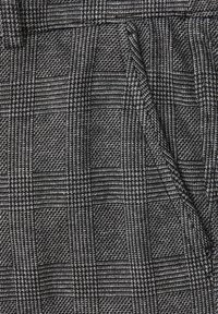 Tissu à motifs pied-de-poule noir et blanc et à carreaux, avec des coutures visibles et un détail de tissage texturé.